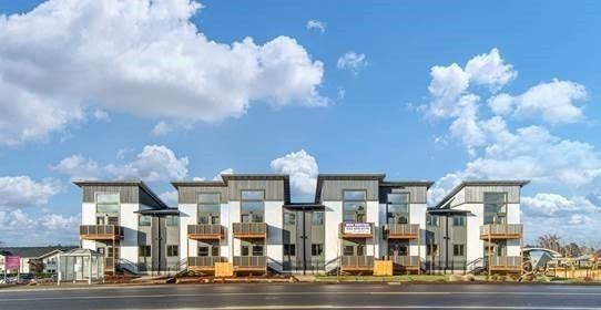 Modern row of townhouses with gray and white facades under a blue sky with clouds
