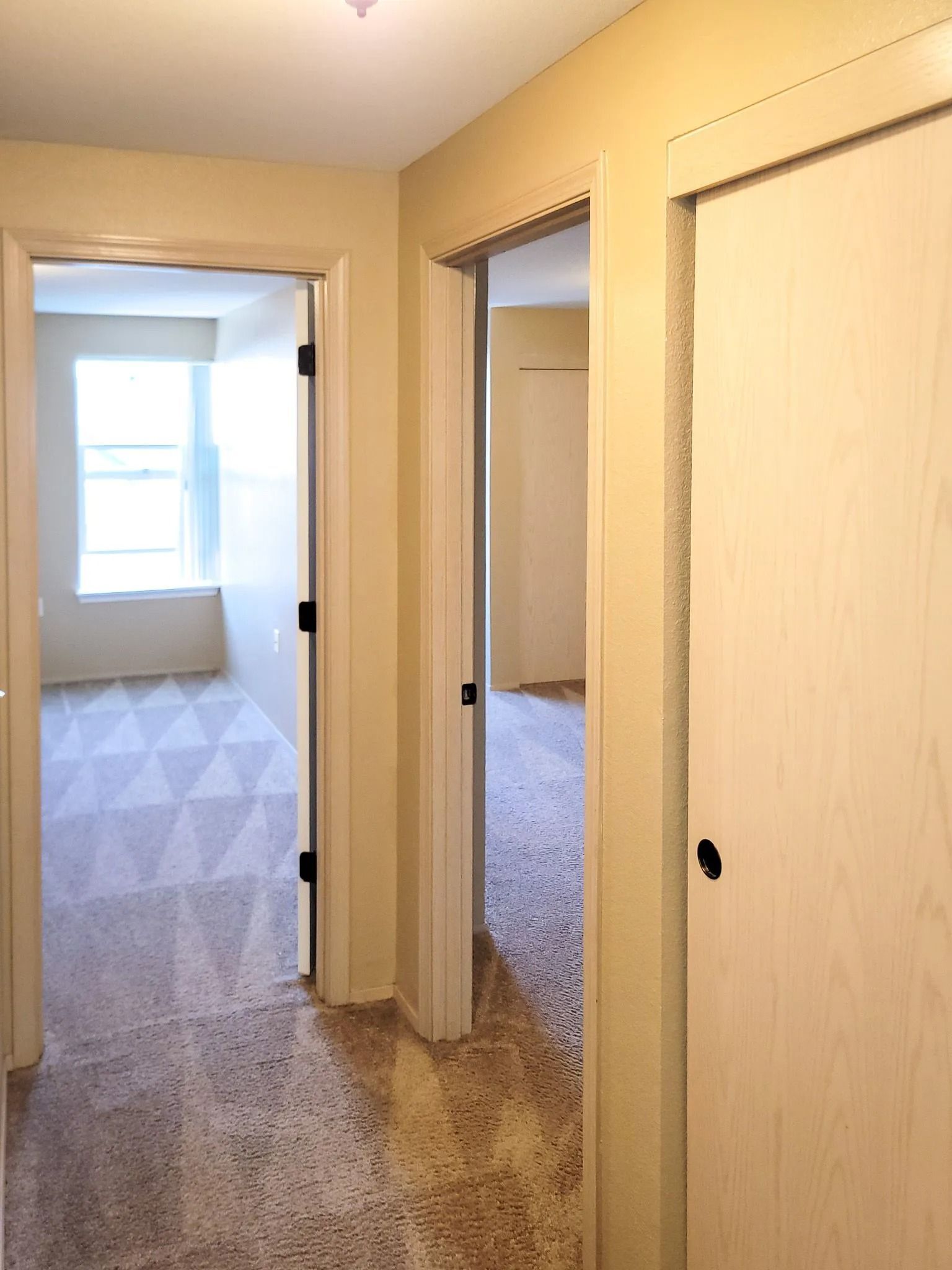 Hallway with three open doorways leading to carpeted rooms and a bright window at the end.