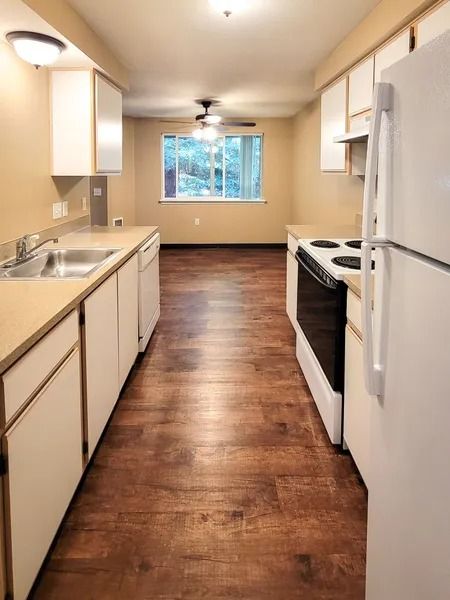 Narrow galley kitchen with white cabinets, wood floors, and a window at the far end.