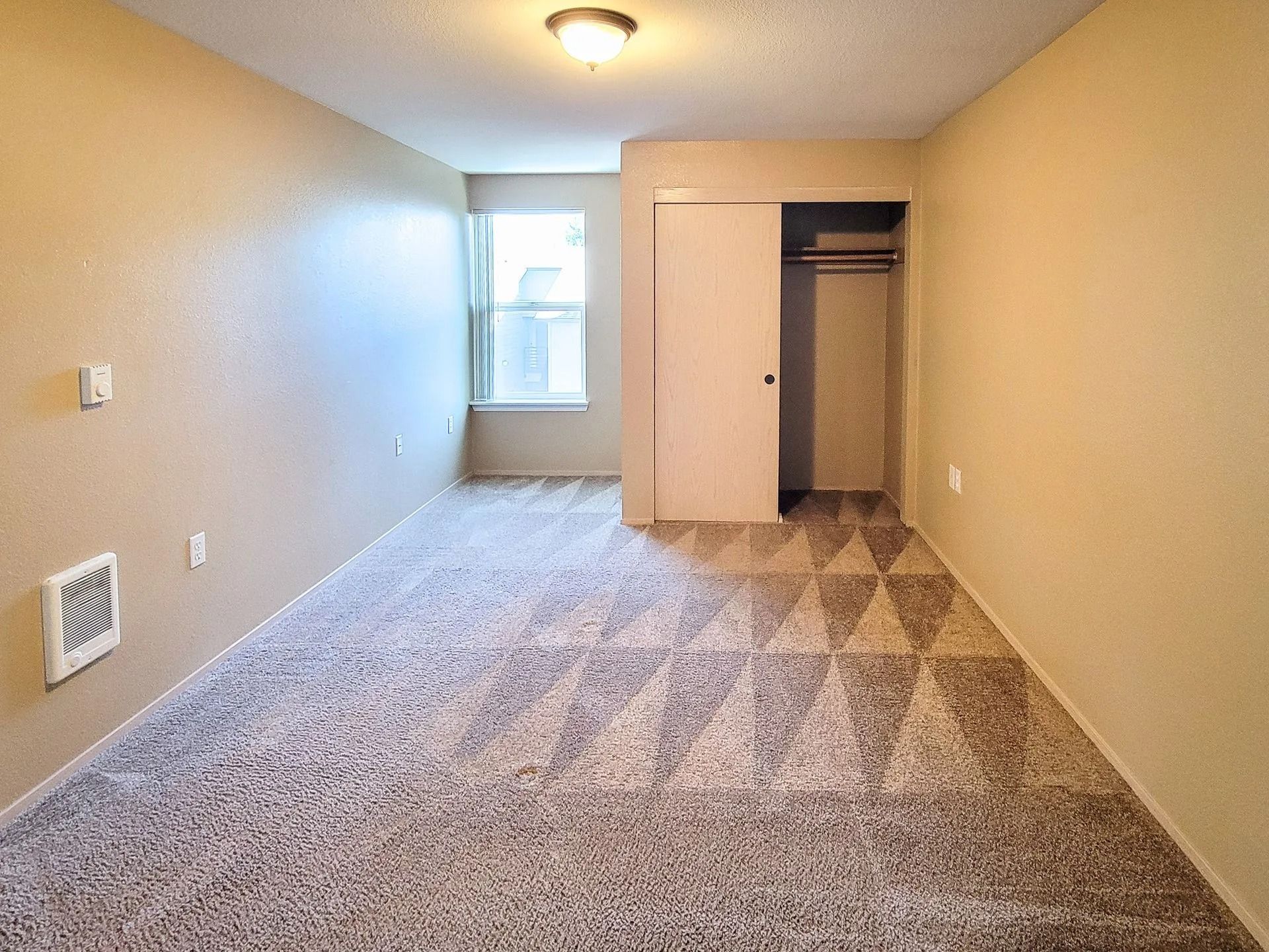 Empty beige bedroom with carpet, closet, and window at the far end