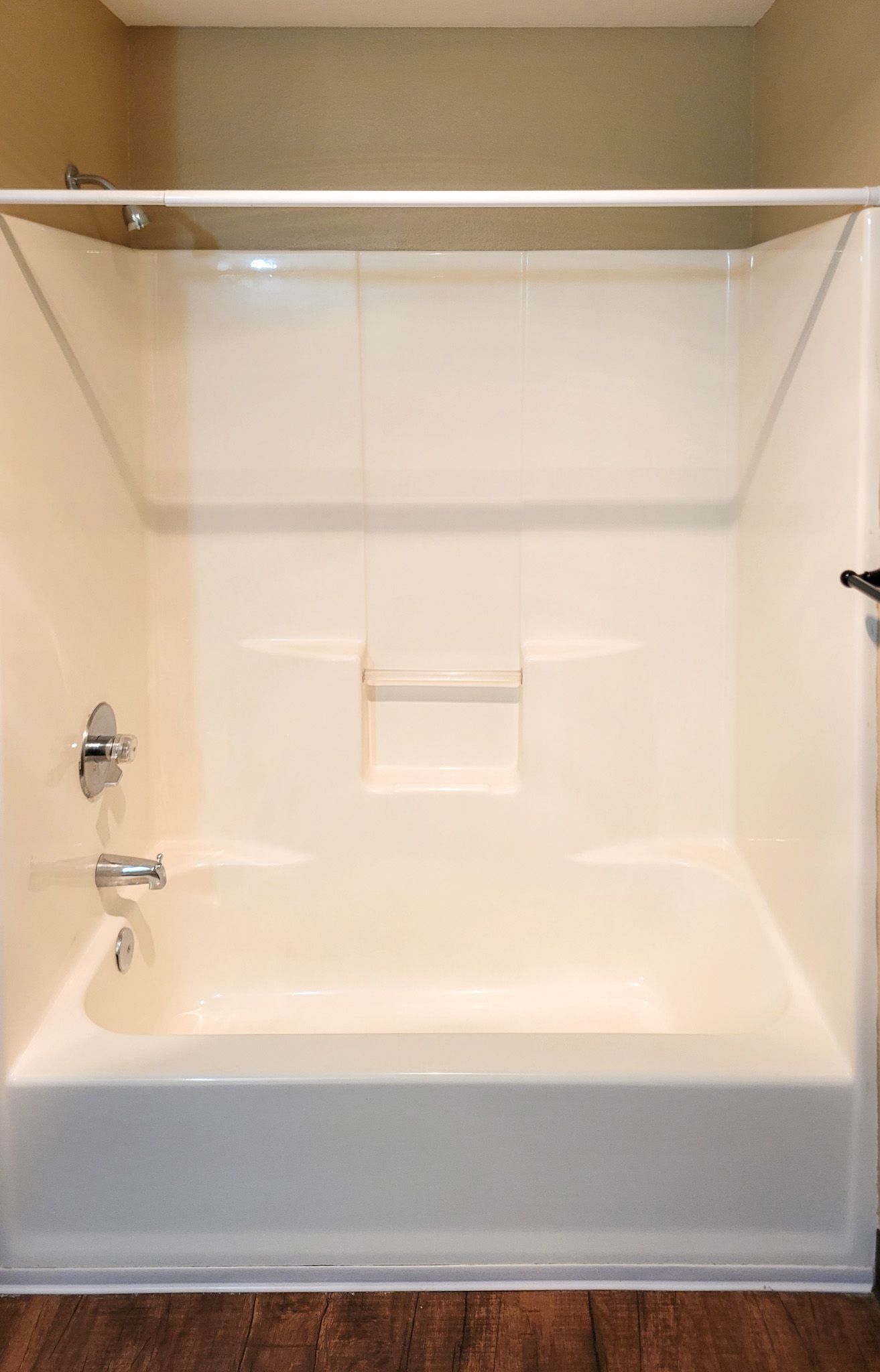 Empty beige bathtub and shower alcove with chrome fixtures and white grab bar.