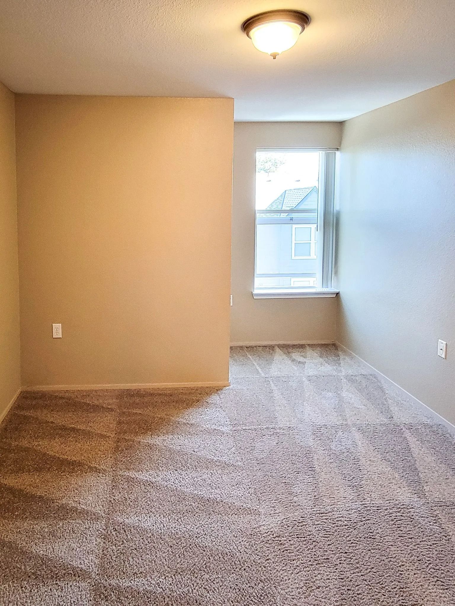 Empty beige room with carpet and a window at the far end