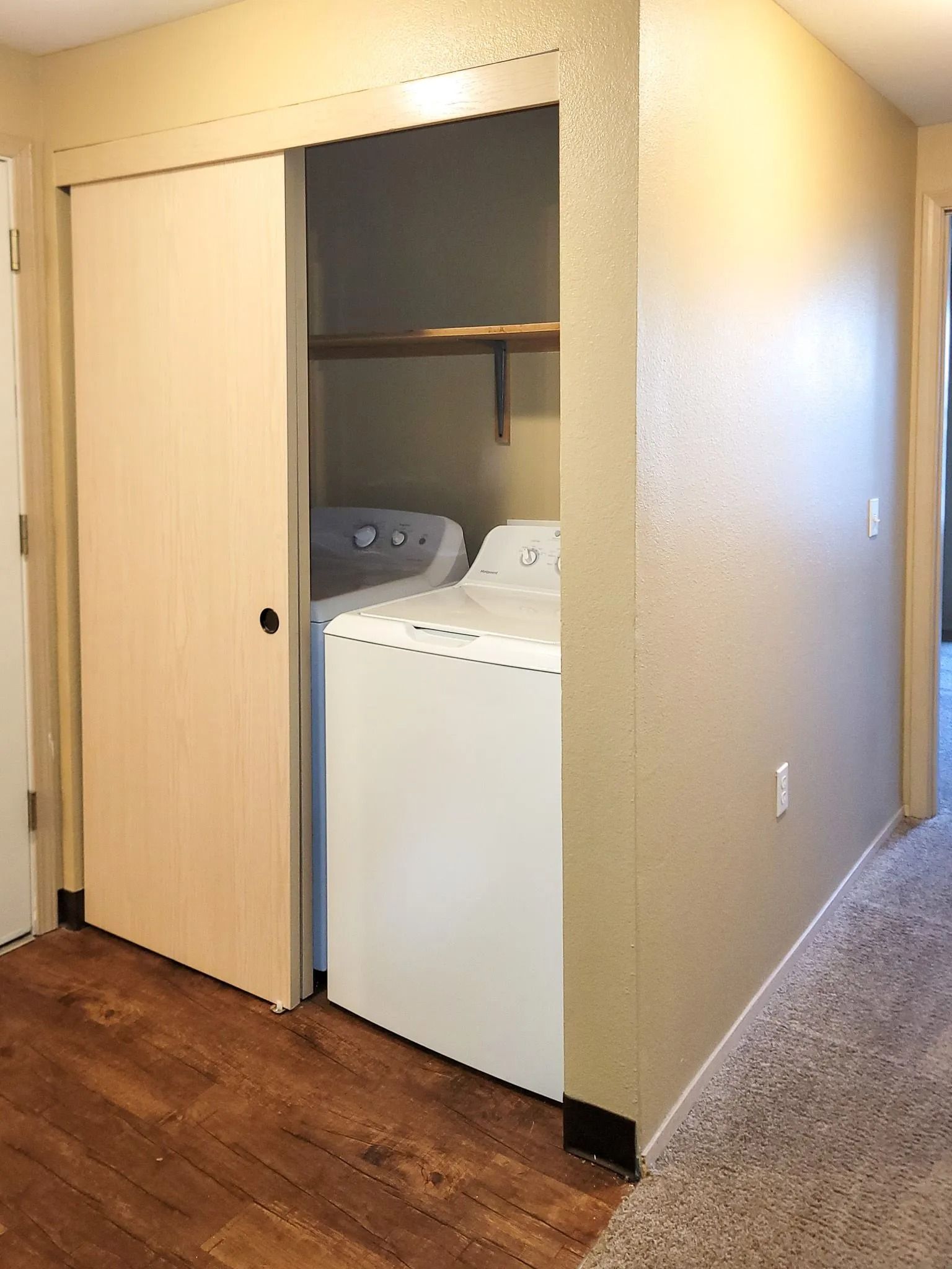 Hallway closet with sliding door open, revealing a washer and dryer inside.