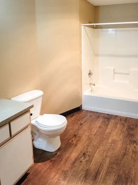 Small bathroom with white toilet, wood floor, beige walls, vanity, and tub/shower combo