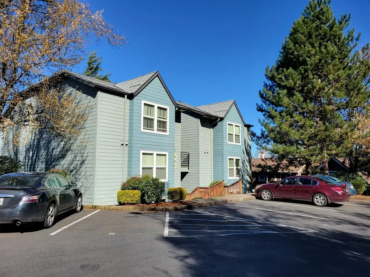 Blue apartment building with parked cars under a clear sky