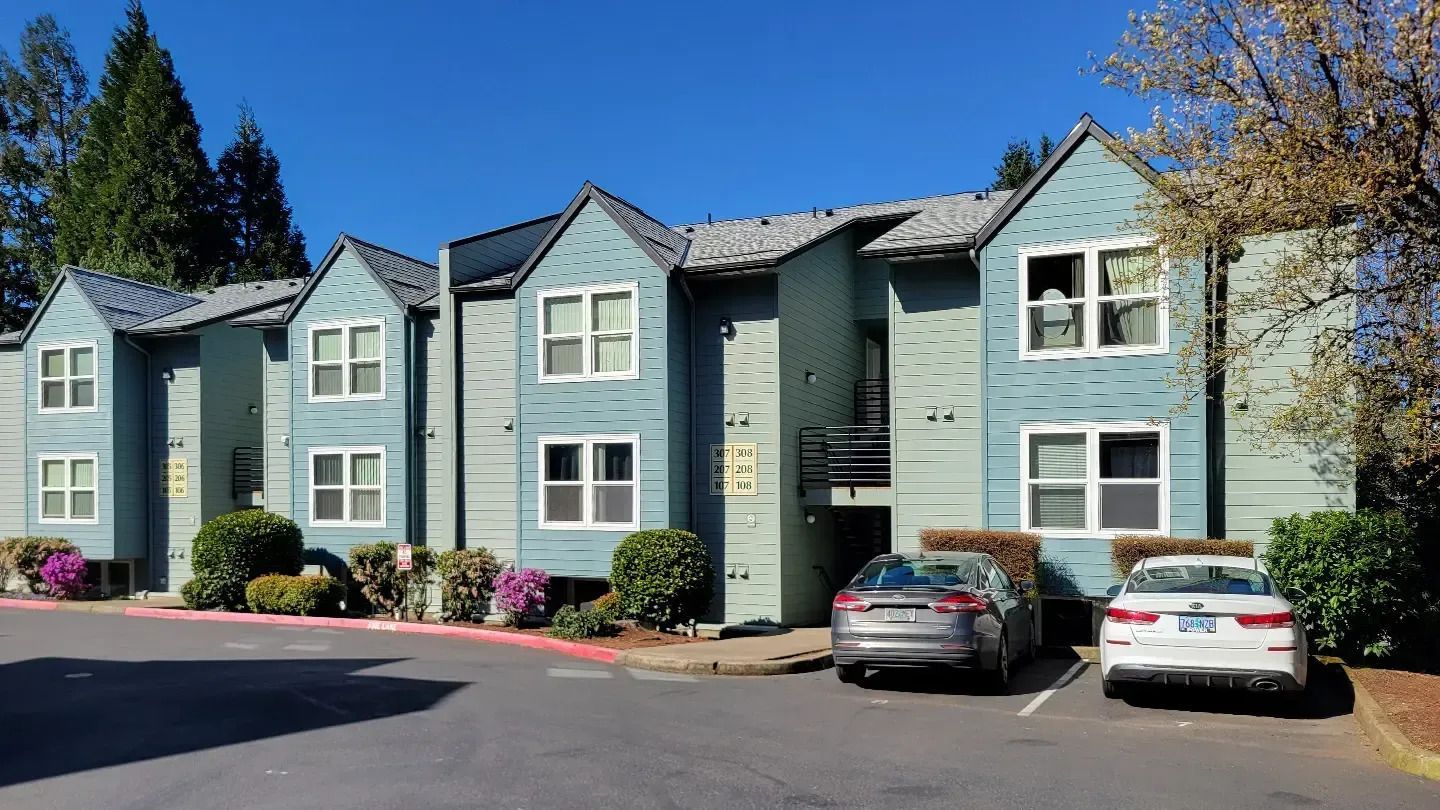 Row of blue-gray apartment buildings with parked cars under a clear blue sky