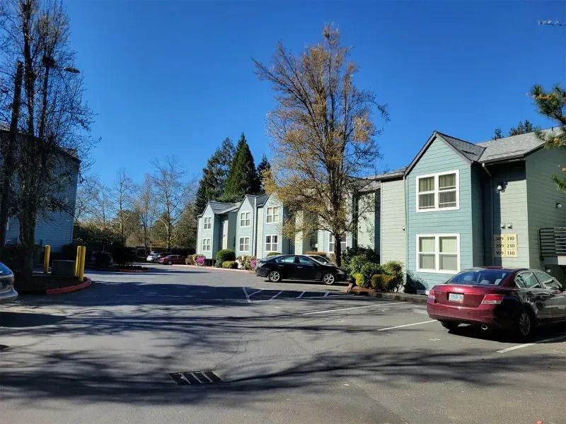 Apartment complex parking lot with parked cars and leafless trees under a clear blue sky