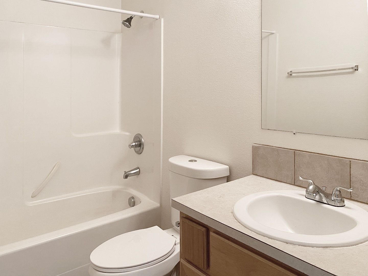 Small bathroom with white tub, toilet, and sink vanity beside a mirror.