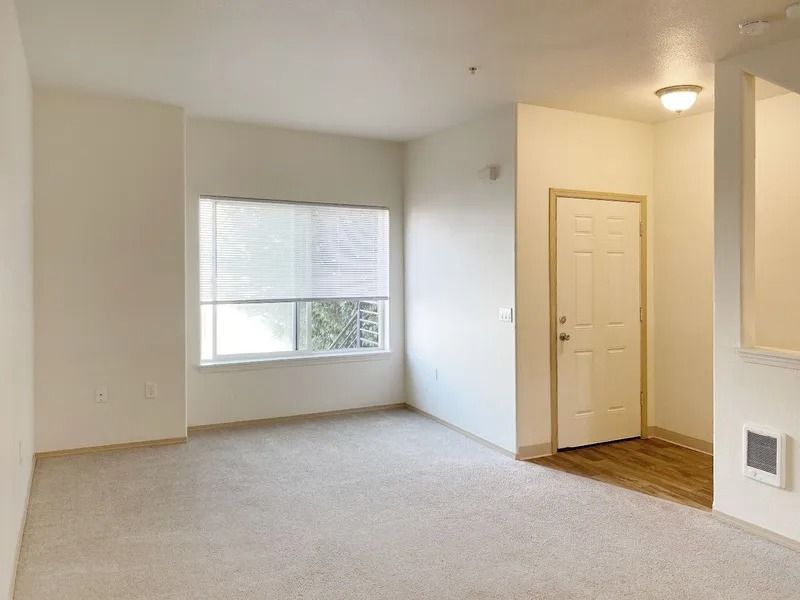 Empty beige living room with window, closet door, and carpeted floor