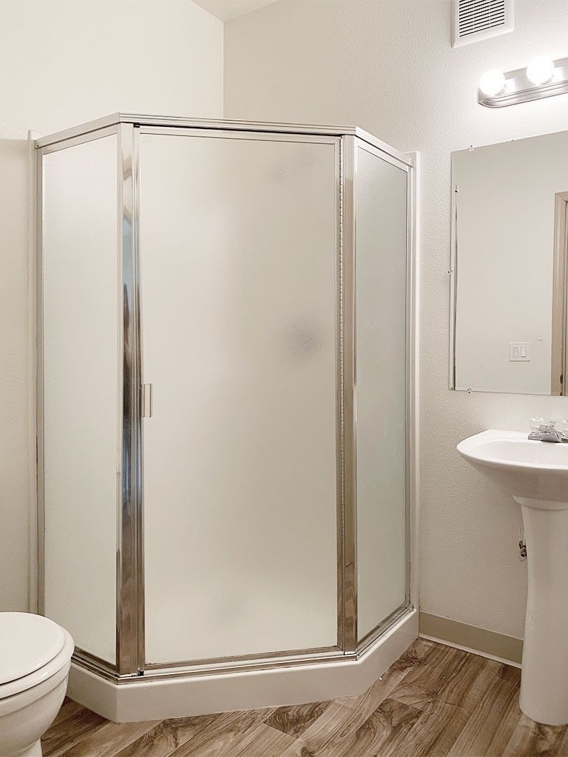 Bathroom with corner glass shower stall, toilet, and wall-mounted sink beside a mirror
