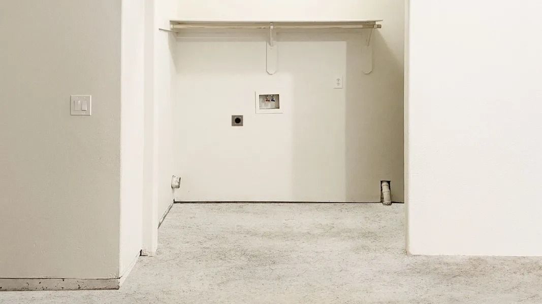 Empty carpeted hallway with a white wall opening and a small dark outlet on the far wall.