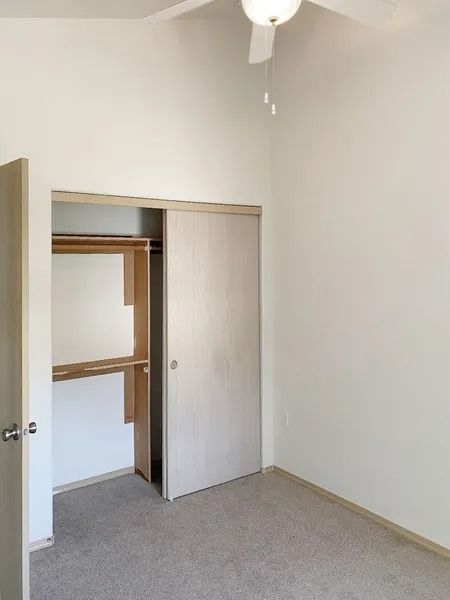 Small empty bedroom with open closet, sliding door, beige walls, and carpeted floor.