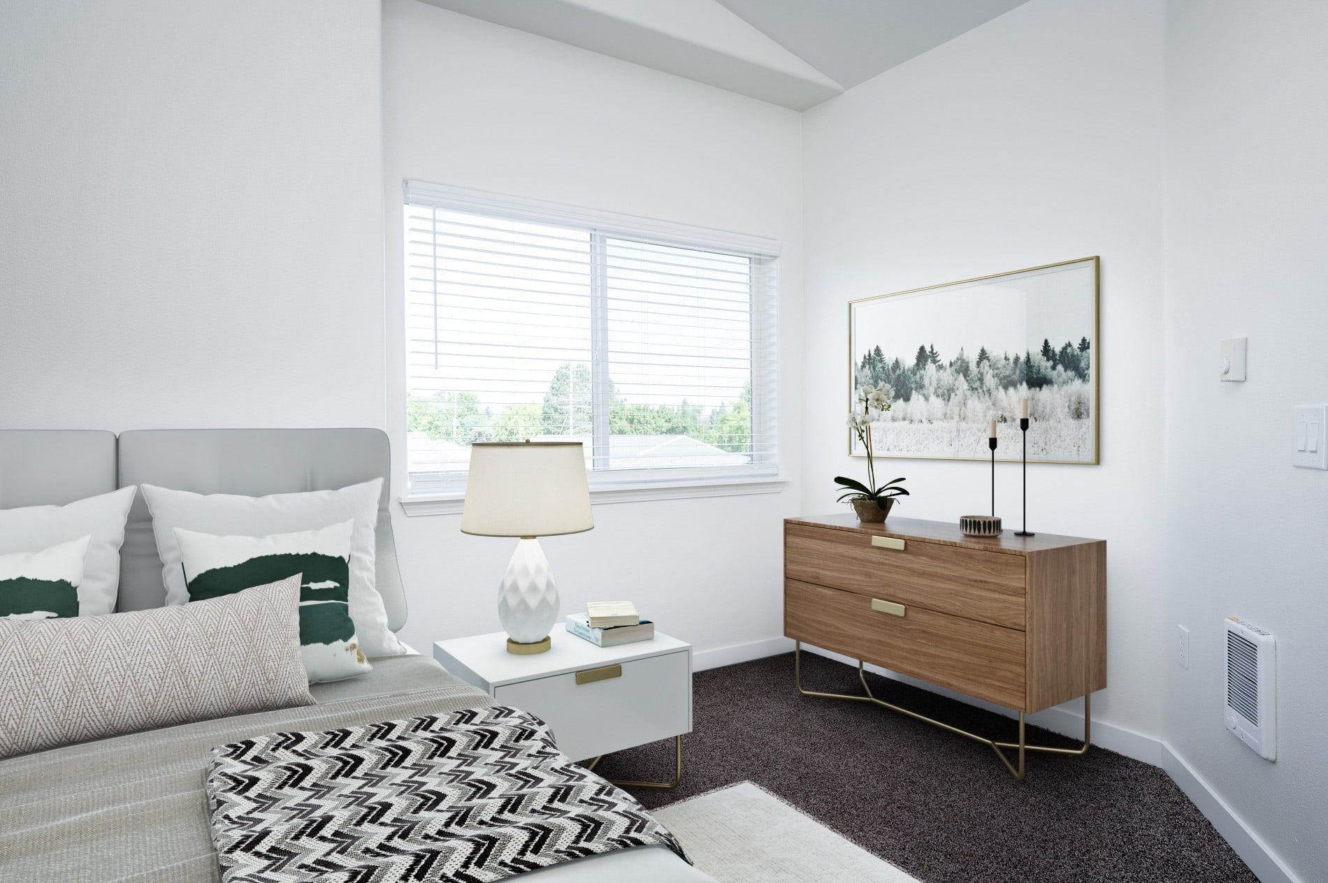 Bright bedroom with a bed, nightstand lamp, window, and wooden dresser with framed art.