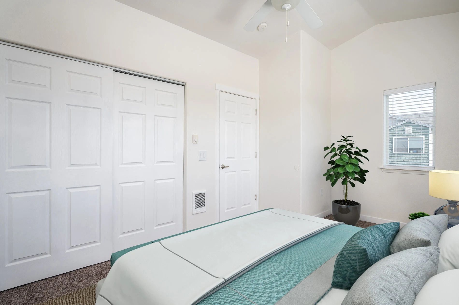 Bright bedroom with white closets, a bed, teal pillows, and a potted plant near a lamp.