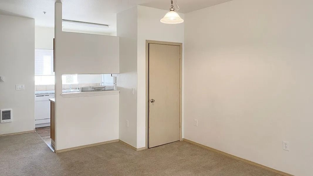 Empty beige room with carpet, white walls, a door, and a hanging light fixture