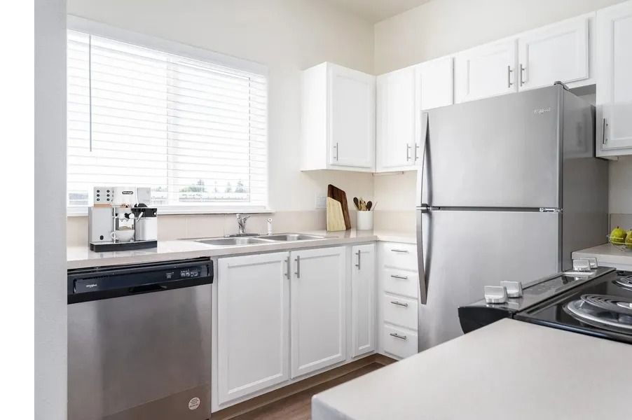 Bright white kitchen with stainless steel appliances, window blinds, and light countertops