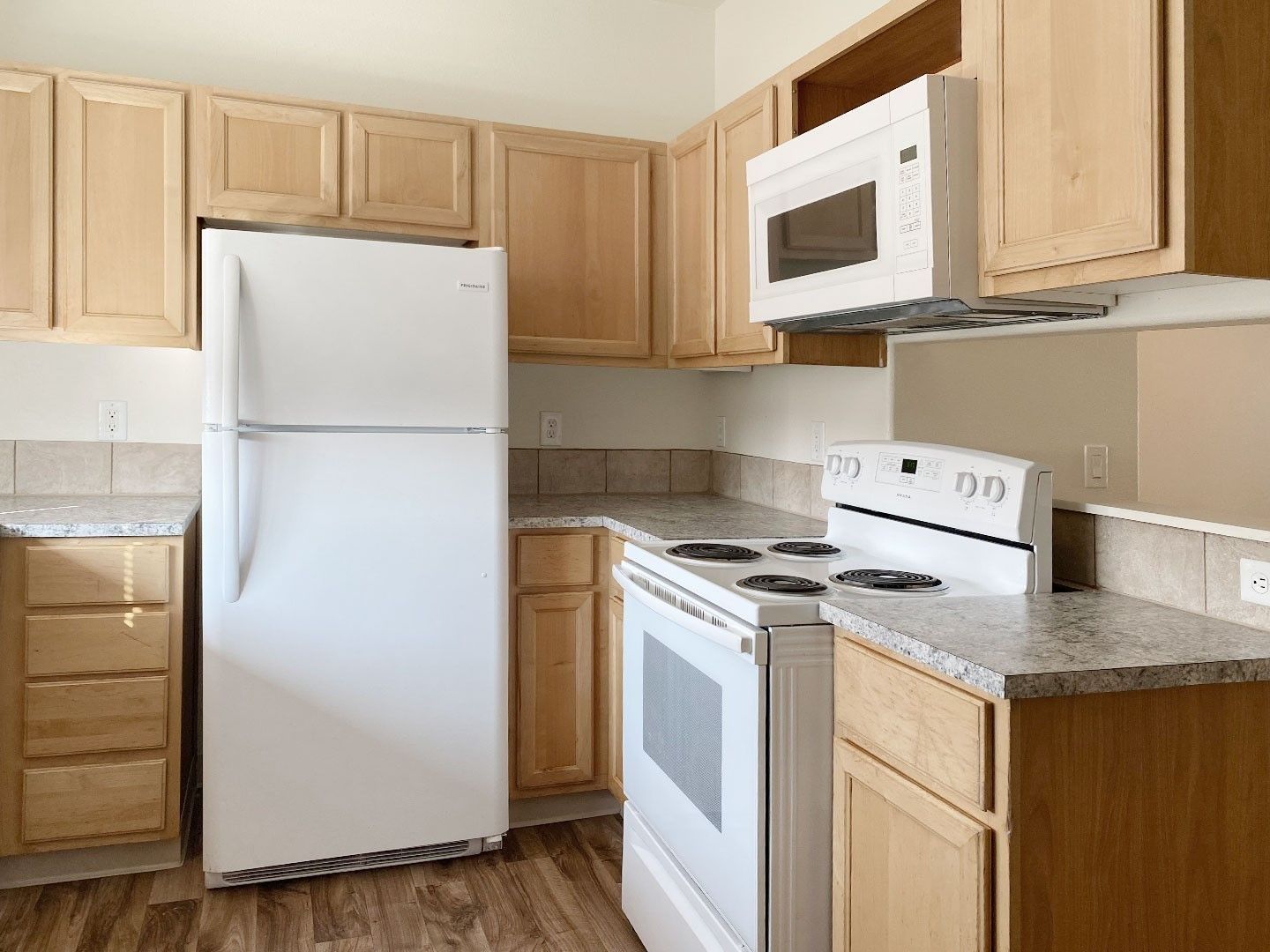 Empty beige kitchen with white appliances and light wood cabinets