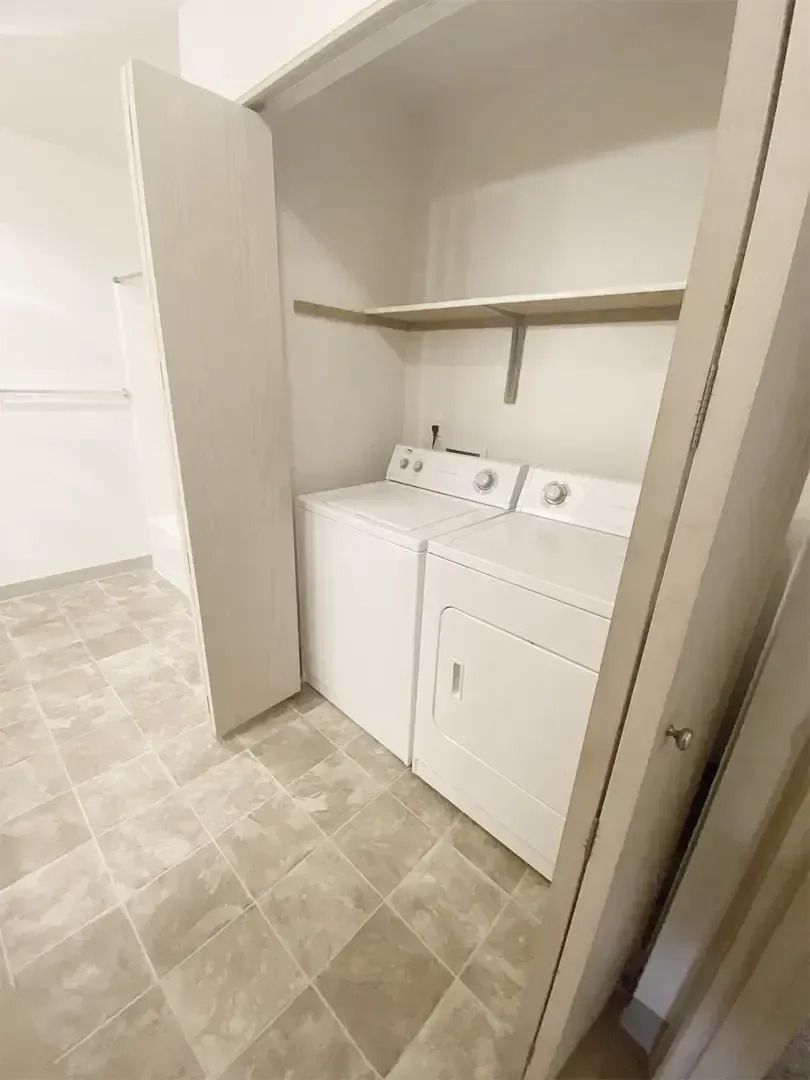 Laundry closet with stacked washer and dryer, white shelving, and tiled floor