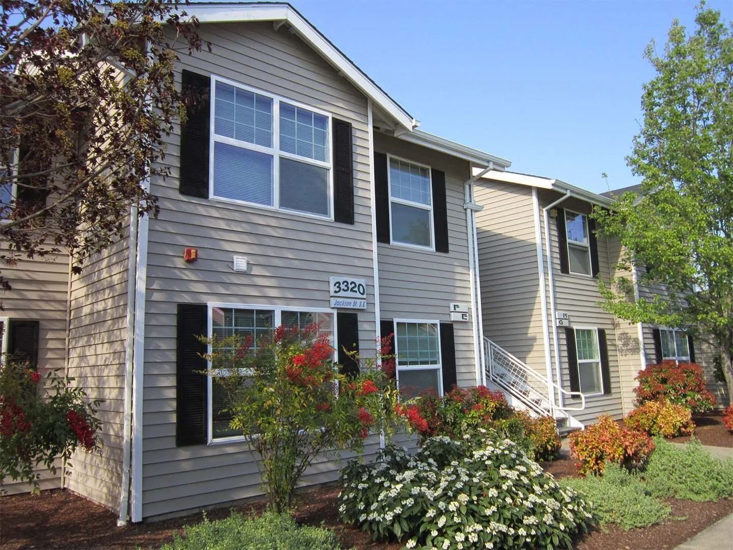 Suburban apartment building with gray siding, black shutters, and landscaped flower beds in front