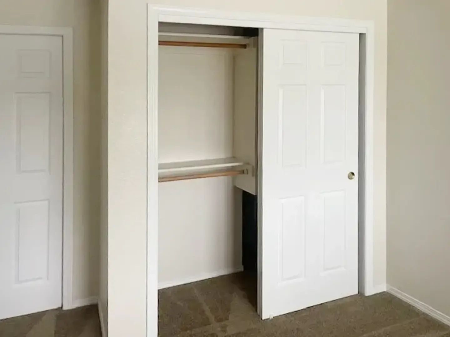 Open closet with sliding white doors, hanging rod, and tiled floor in a small room.