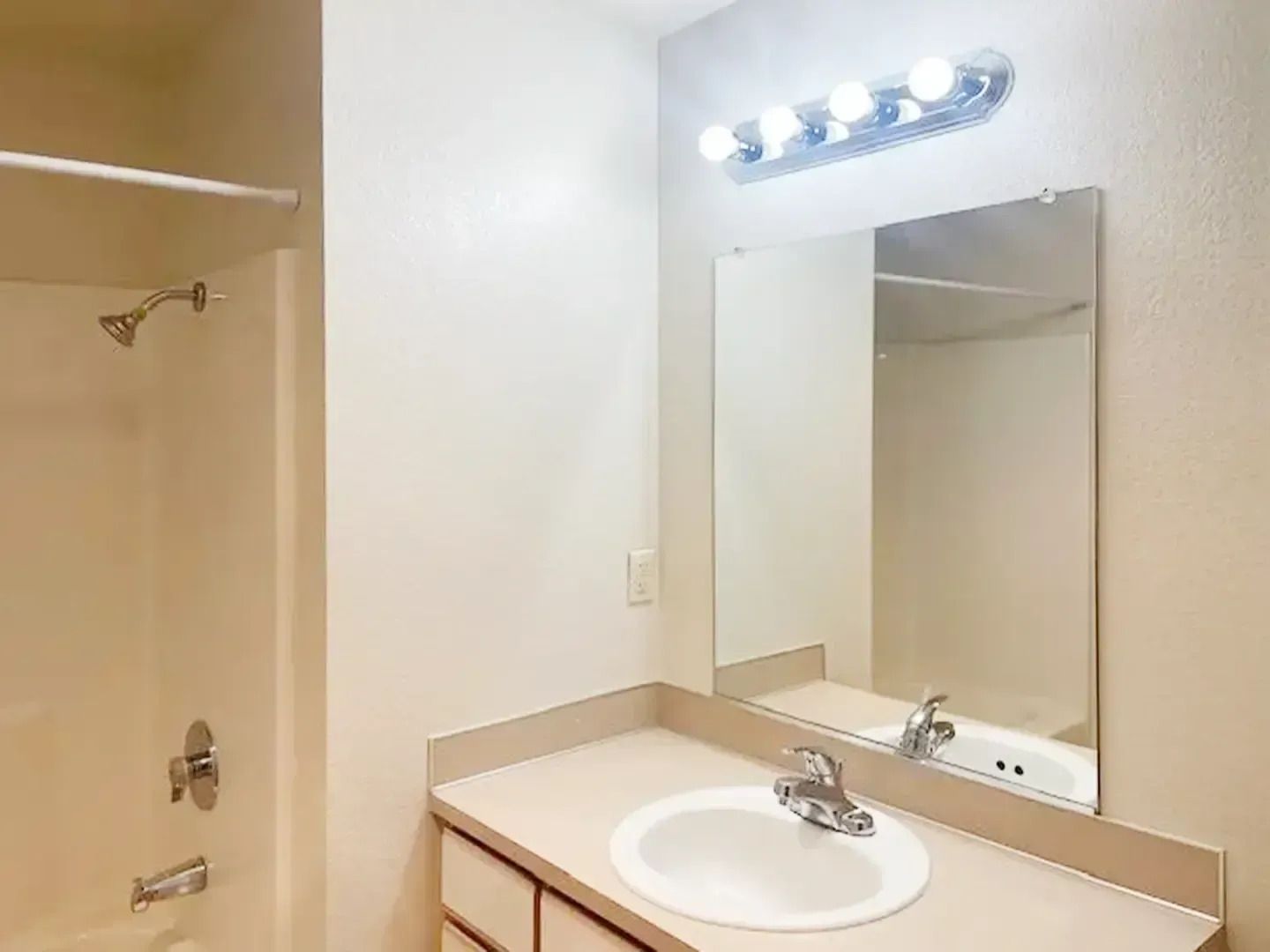 Bathroom vanity with white sink, beige countertop, wall mirror, and bright light fixture.