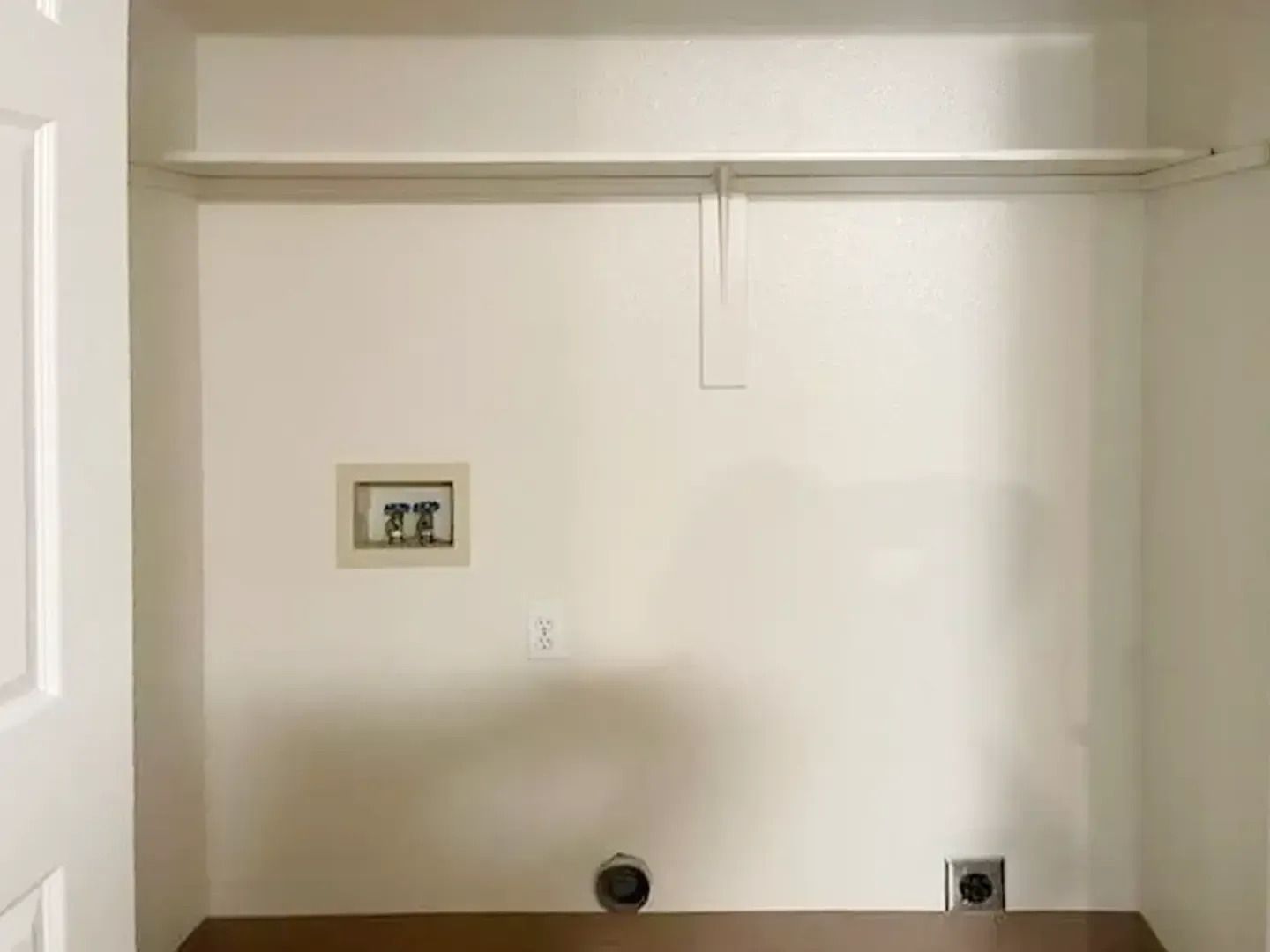 Empty white closet with a shelf, hanging rod, and wall outlets near the floor
