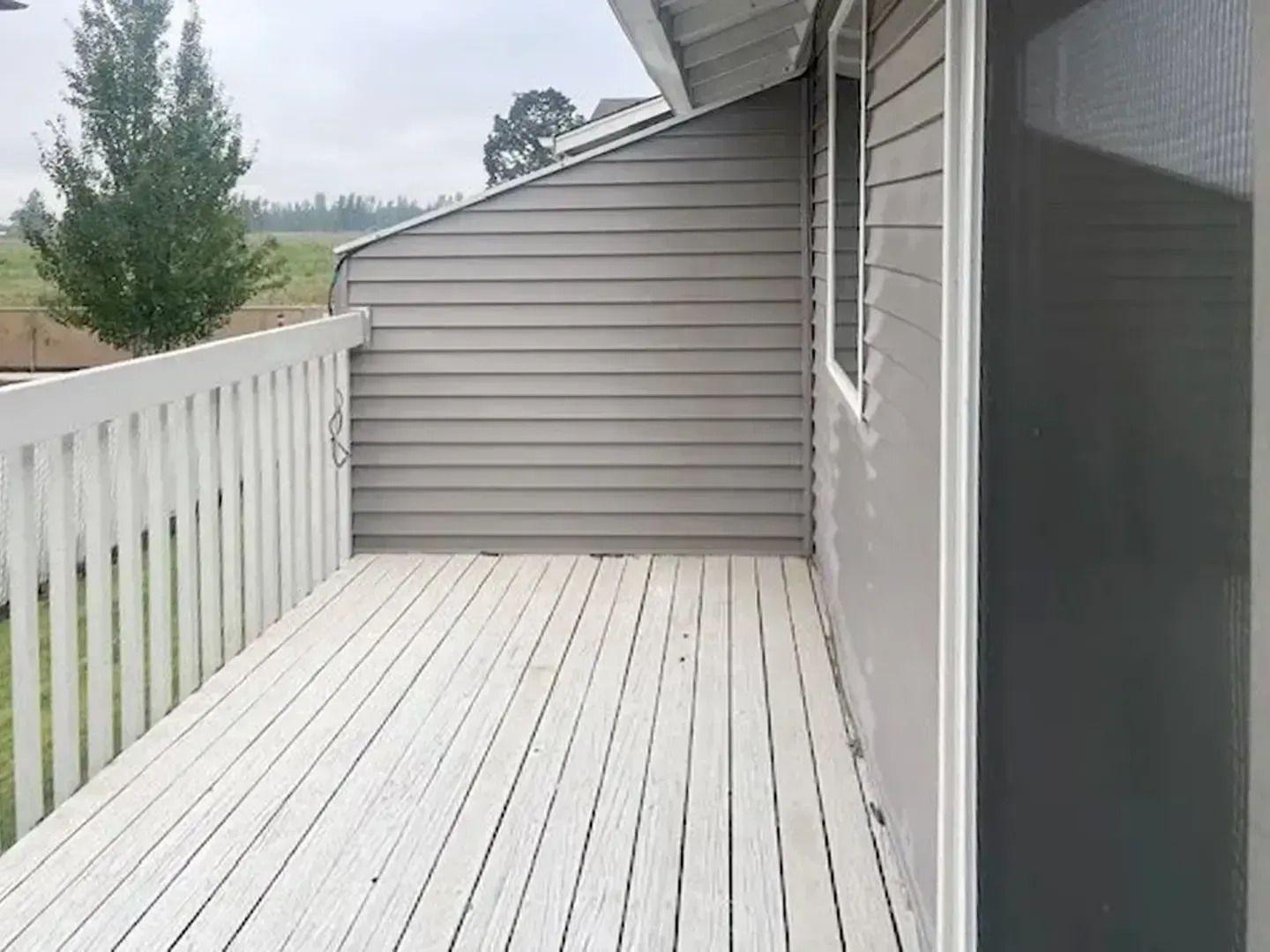 Empty white wooden deck beside a gray house, with white railing and overcast yard view.
