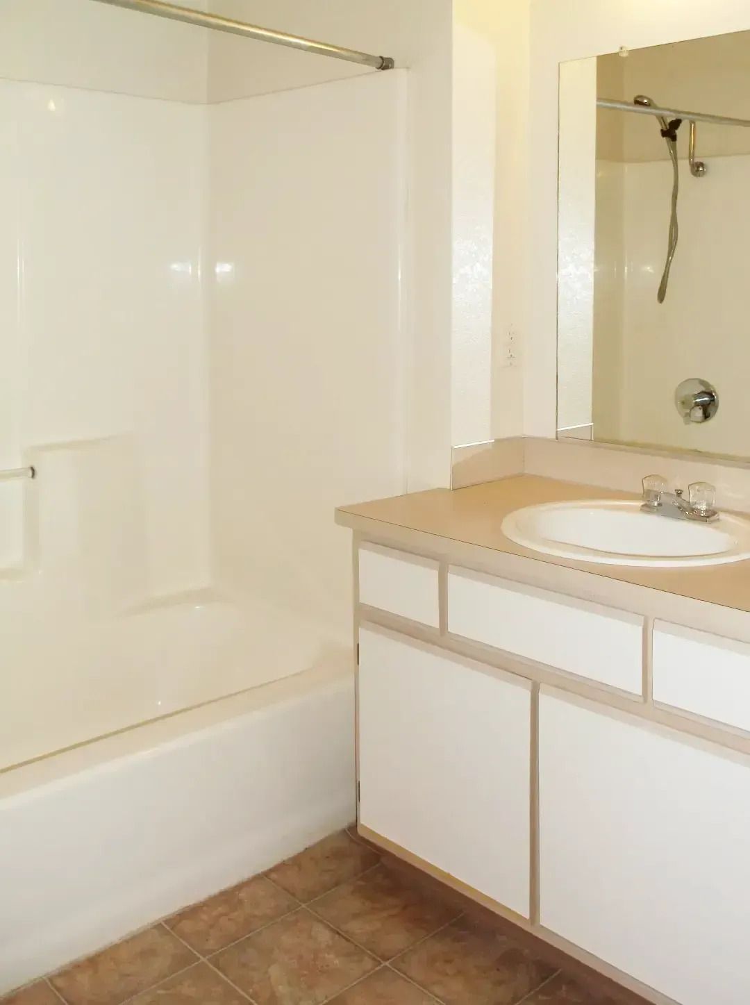 Bathroom with white tub, sink vanity, mirror, and brown tile floor.