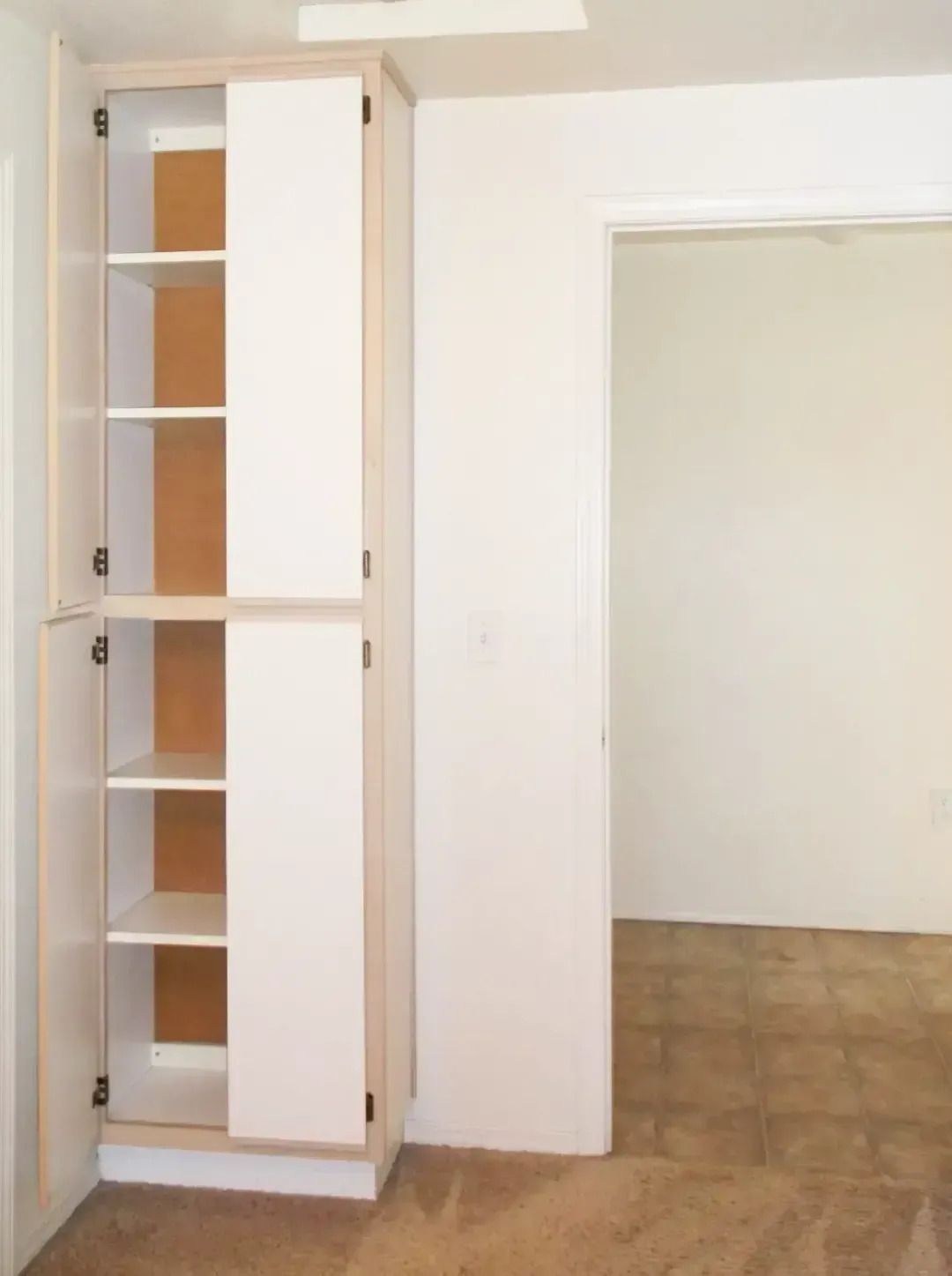 White built-in closet with open shelving beside an empty doorway in a beige room.