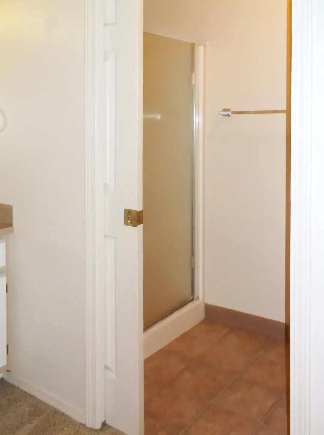Small bathroom entry with open door, beige tile floor, towel bar, and shower stall visible.