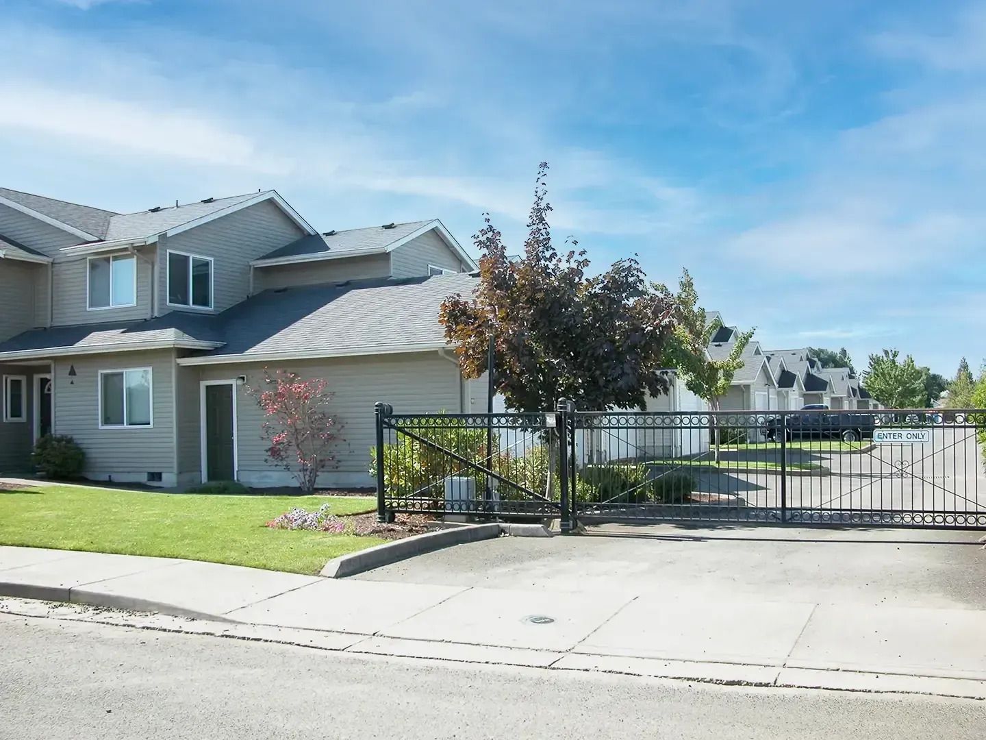 Residential house with gated driveway and front lawn under a clear blue sky