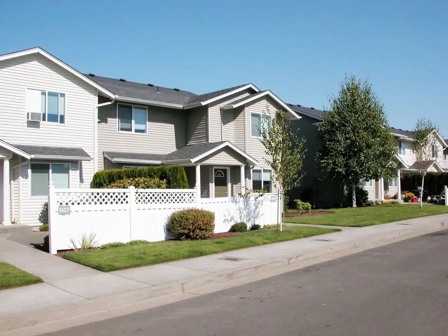 Row of light-gray suburban townhouses with white fencing along a quiet street