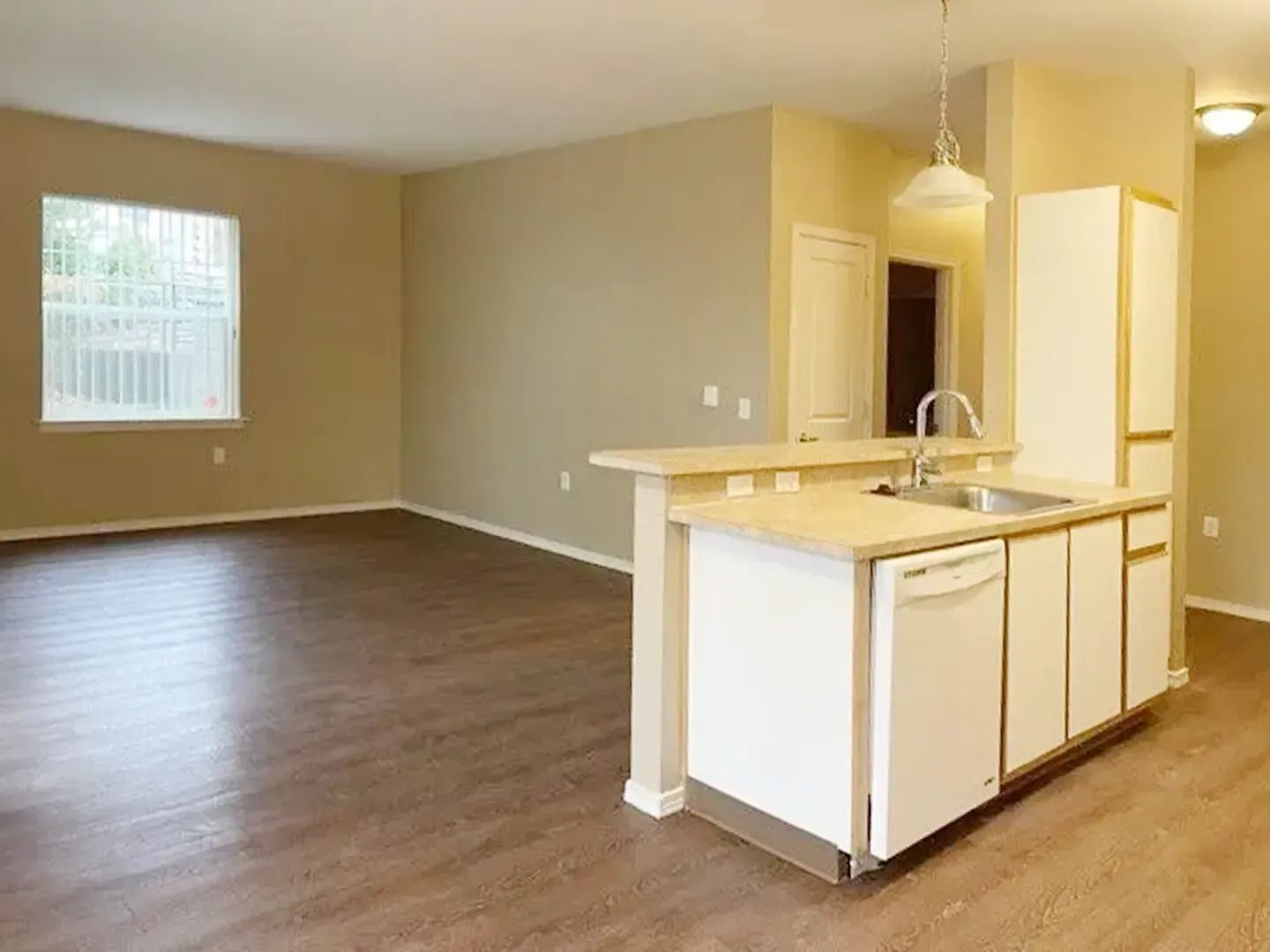 Empty open-plan living room with hardwood floors and a small kitchen island in beige tones