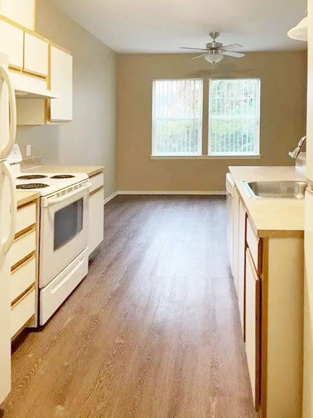 Empty kitchen with white appliances, wood floor, and a windowed dining nook.
