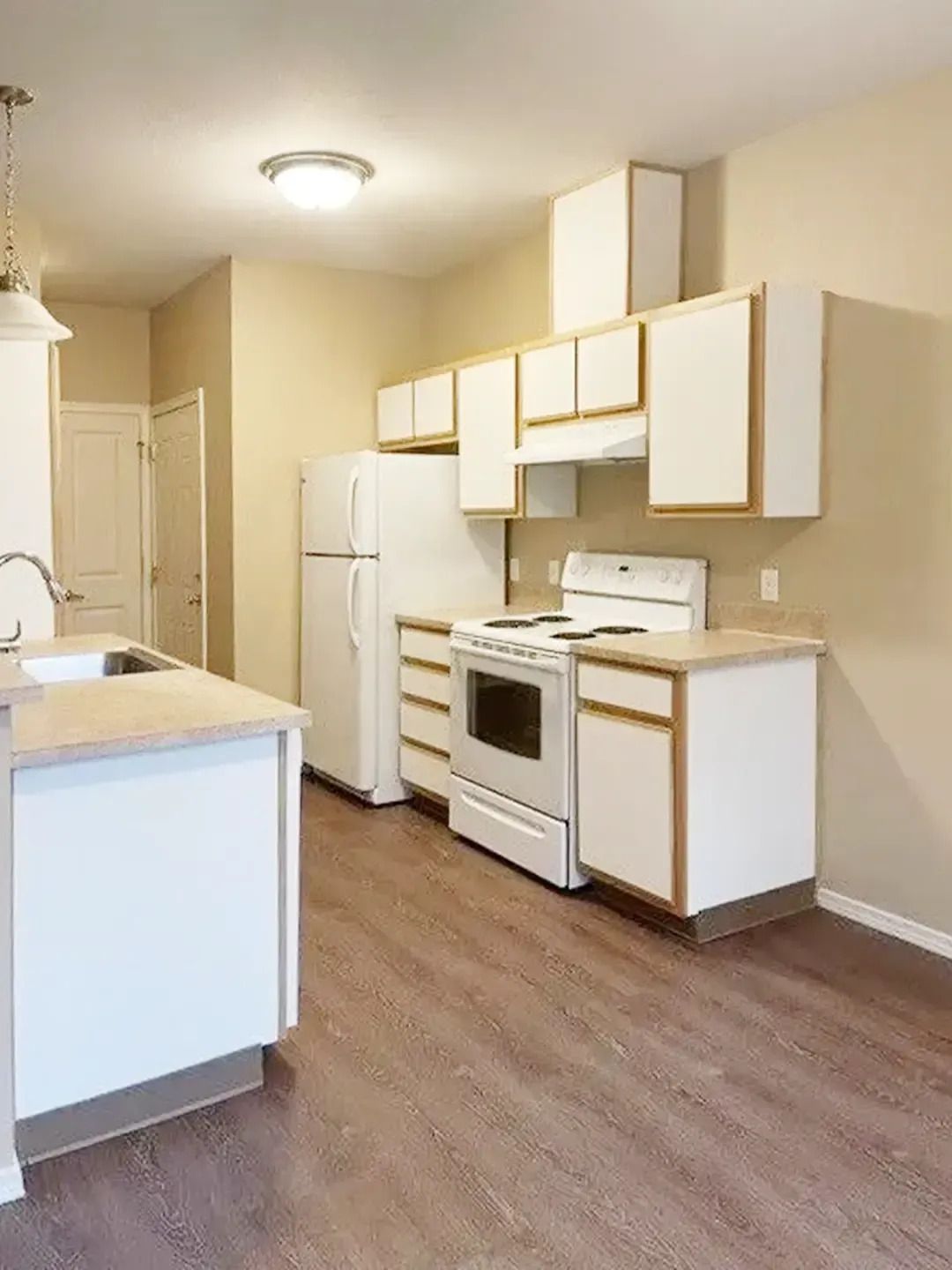 Empty beige kitchen with white appliances, cabinets, and wood-look flooring