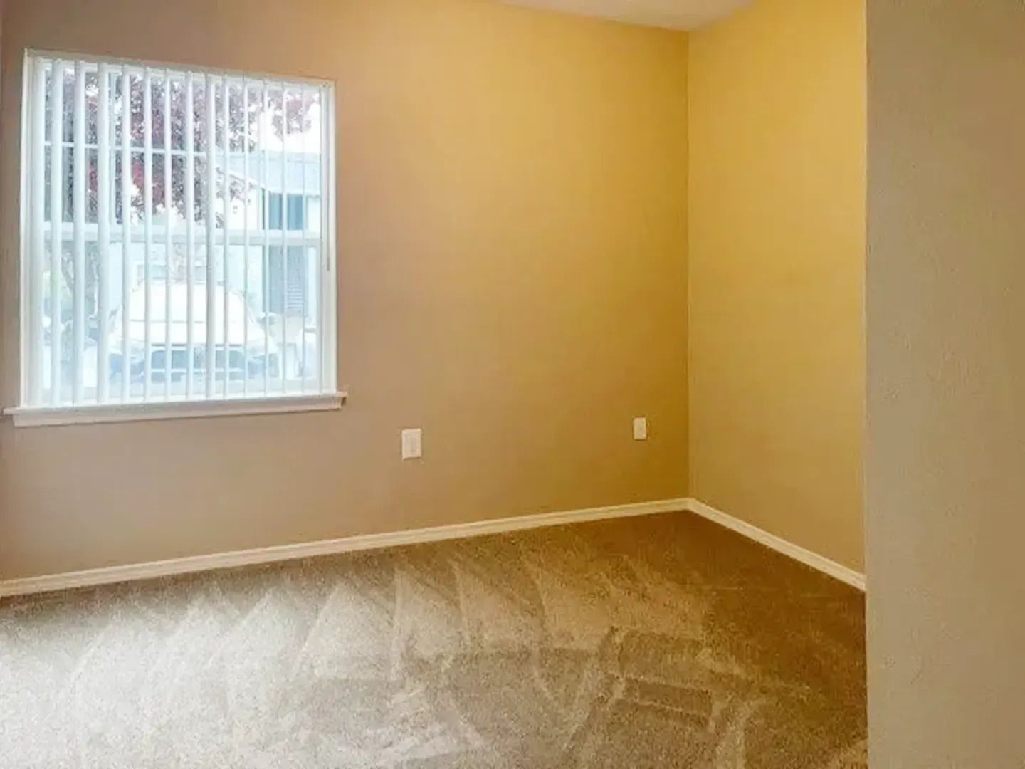 Empty beige bedroom with window blinds and carpeted floor