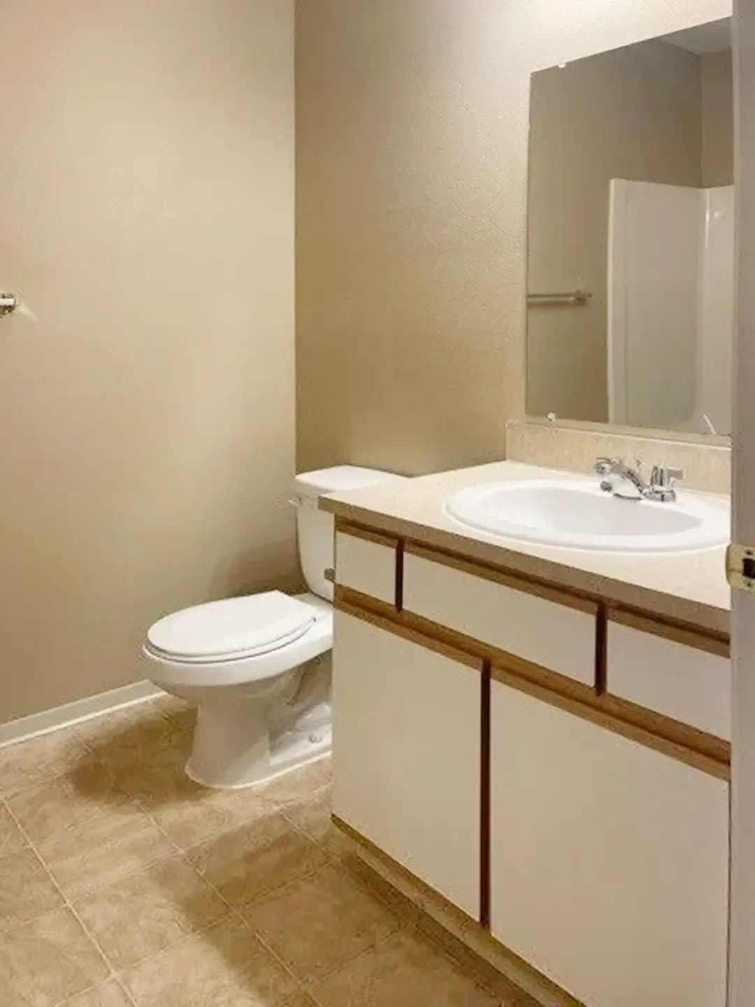 Small beige bathroom with toilet, vanity sink, and mirror.