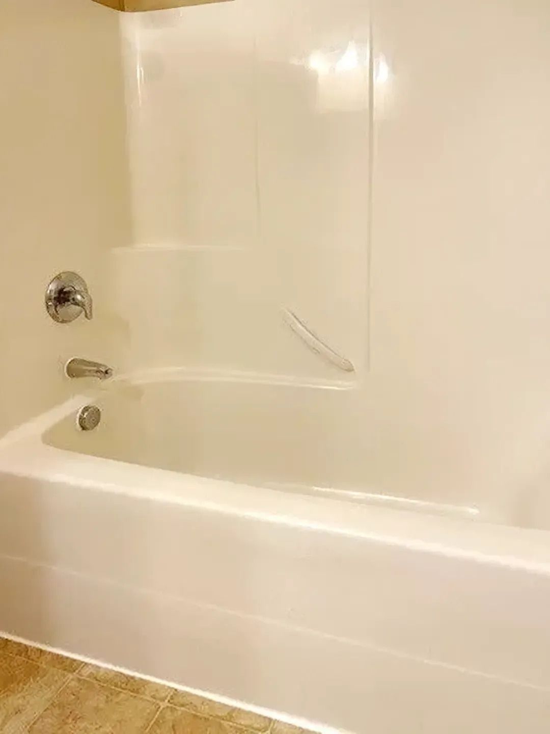 White bathtub and shower surround in a beige bathroom with chrome fixtures