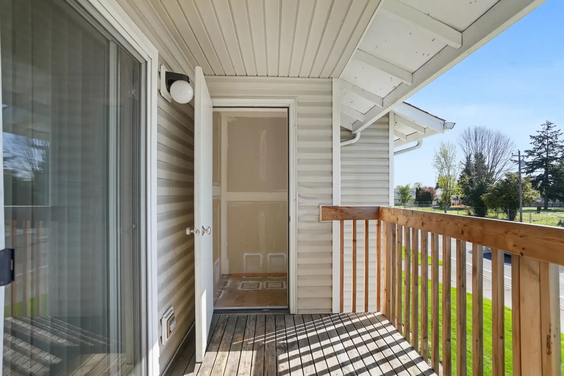 Covered front porch with white siding, wood railing, and a sliding glass door.
