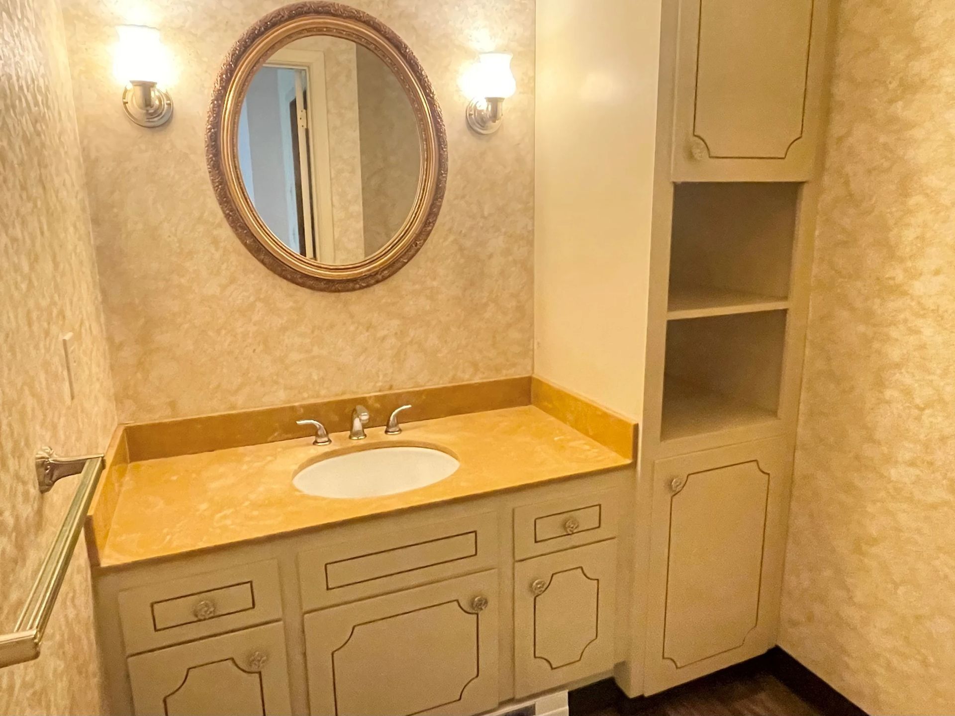 Bathroom vanity with oval mirror, twin sconces, and built-in cabinets in a beige stone countertop setup