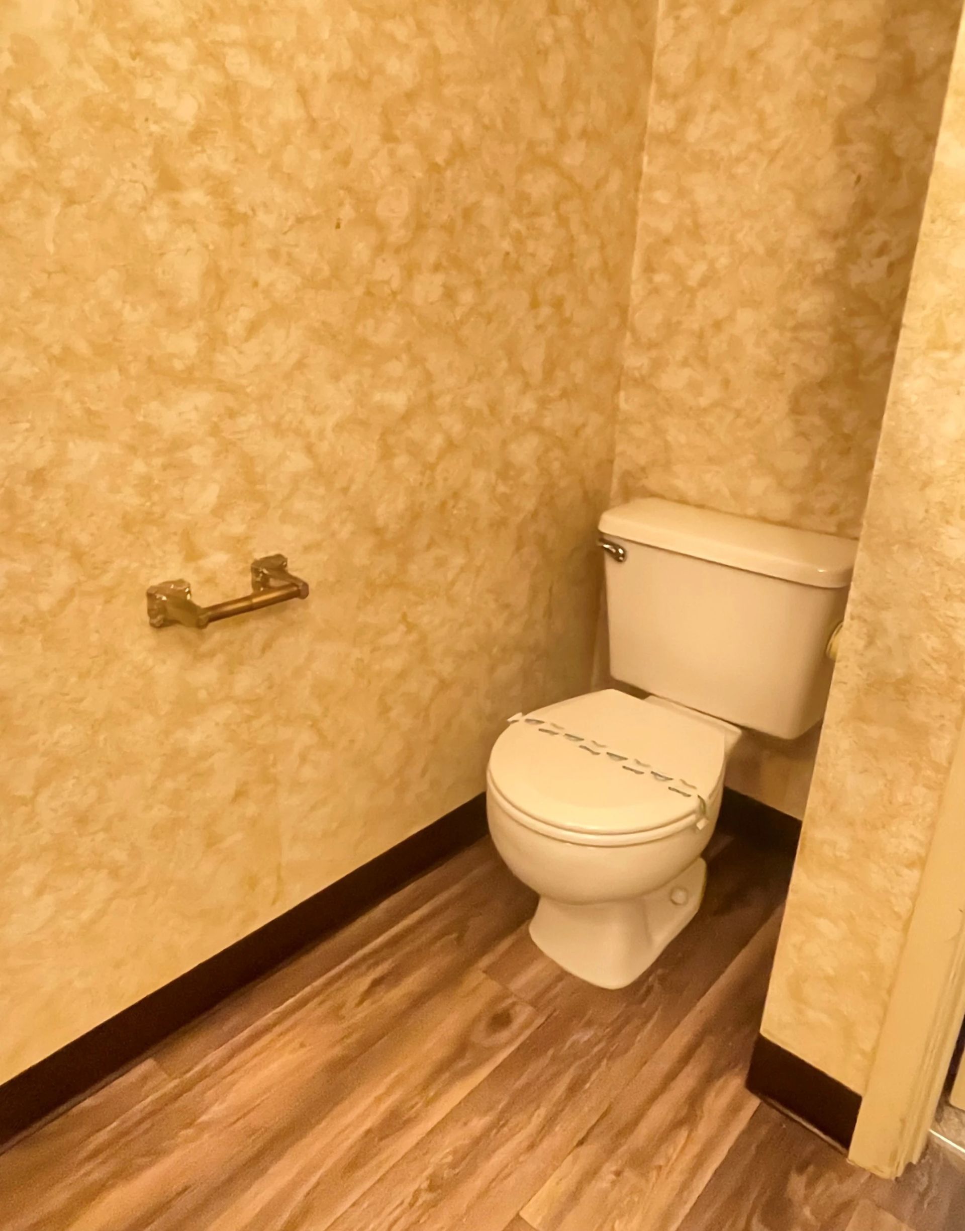 Small beige bathroom with a toilet, wood-look floor, and toilet paper holder on the wall