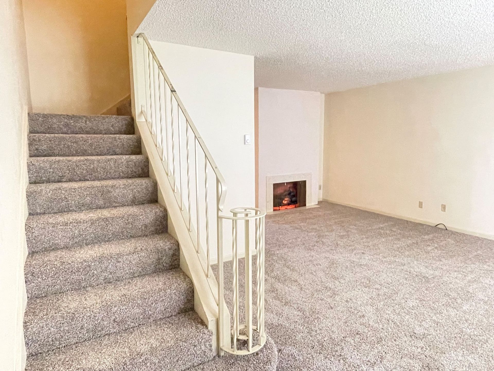 Carpeted staircase beside a living room with a white fireplace and beige walls