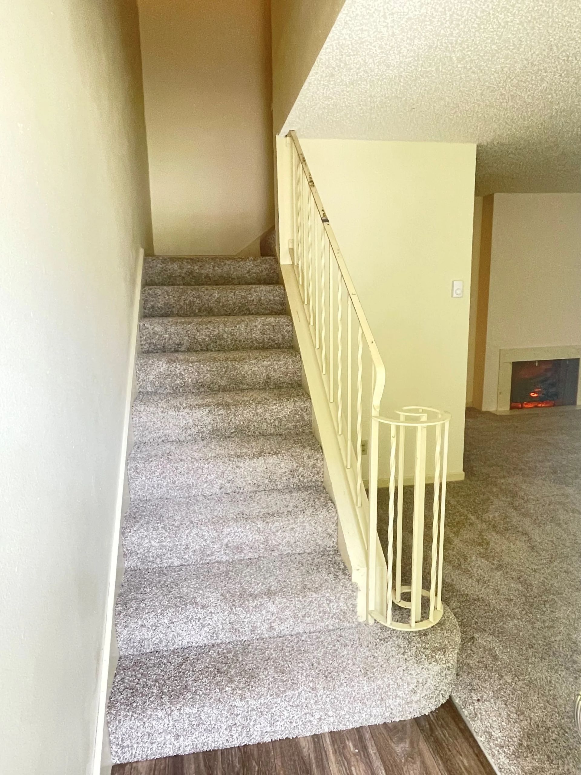 Carpeted staircase beside a beige wall and railing, leading up to a landing in a home hallway.
