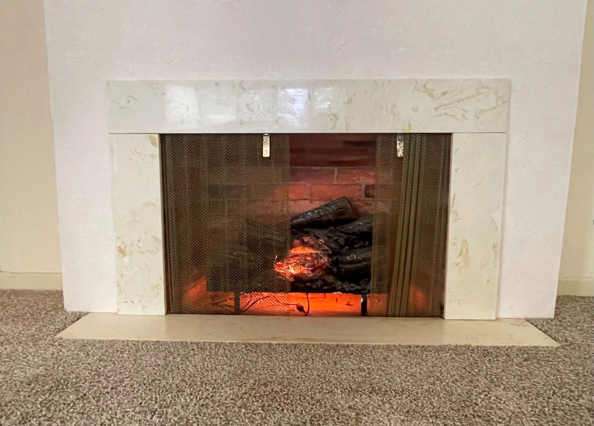 White marble fireplace with a lit fire and stack of logs in a beige-carpeted room