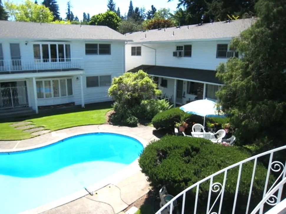 Courtyard apartment complex with swimming pool, white buildings, and patio seating in bright sunlight