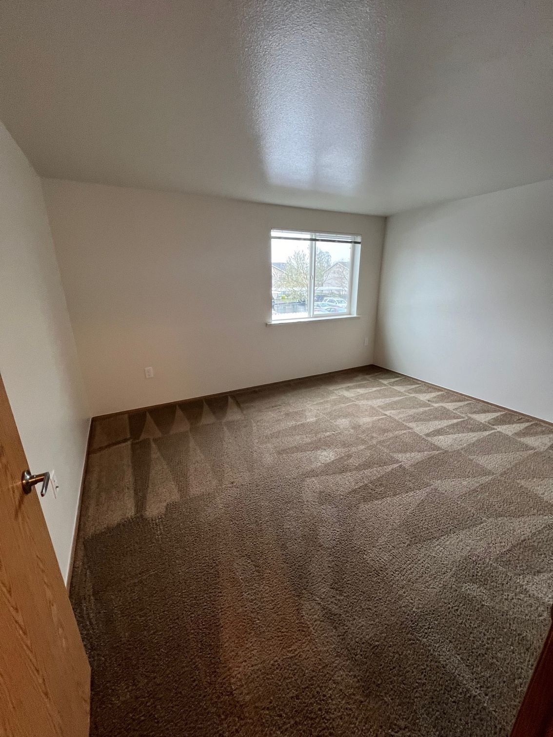 Empty beige bedroom with brown carpet and a small window.