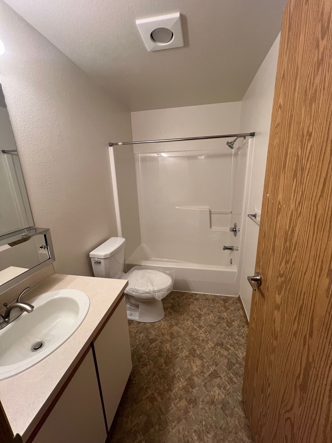 Small bathroom with sink, toilet, and shower/tub; beige walls and wood door.