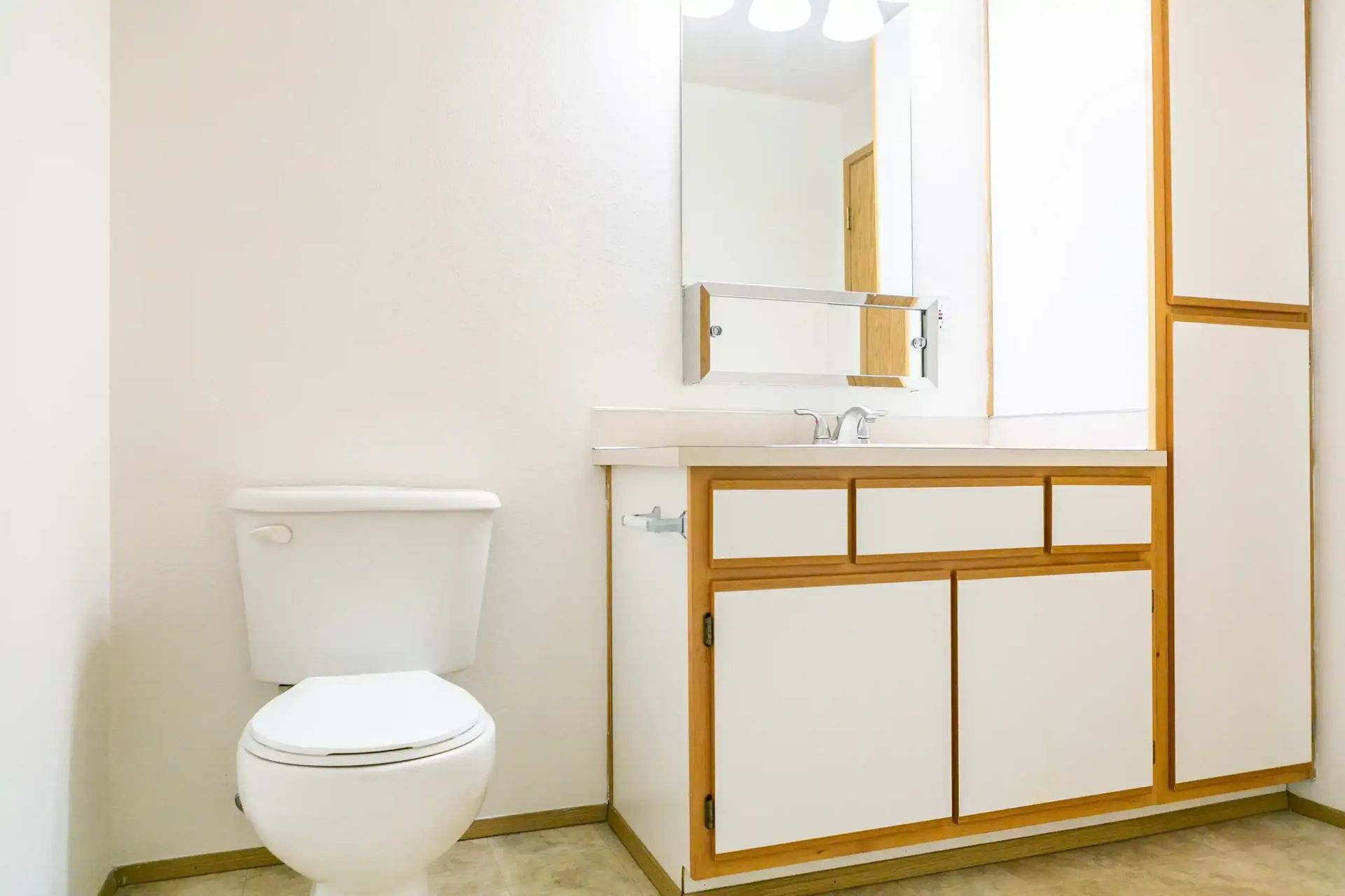 Modern white bathroom with a toilet, sink, mirror, and light wood cabinetry