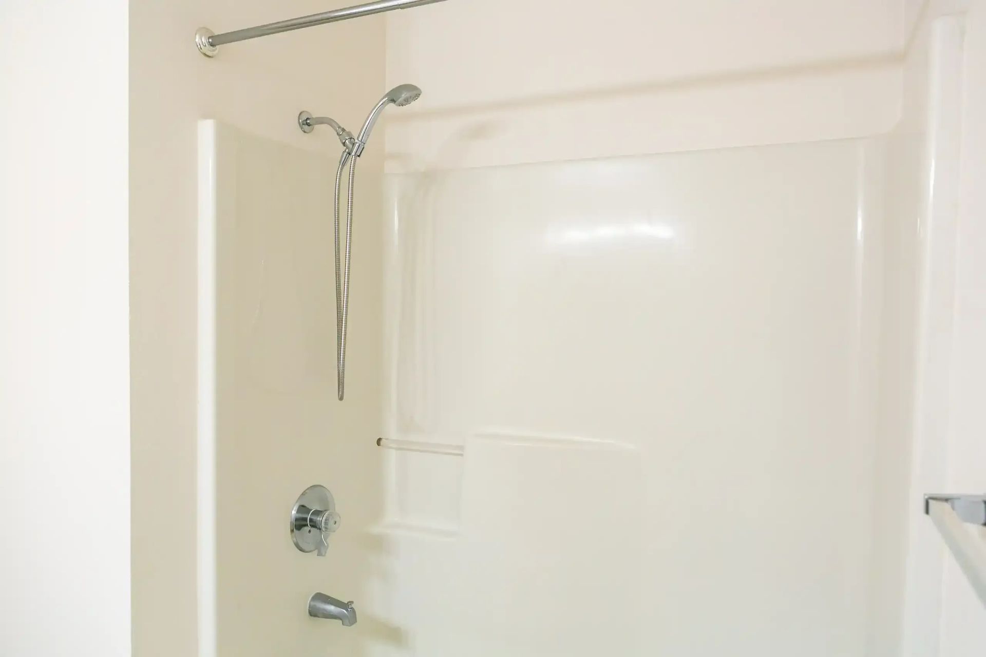 White shower stall with chrome showerhead and tub fixtures against beige walls