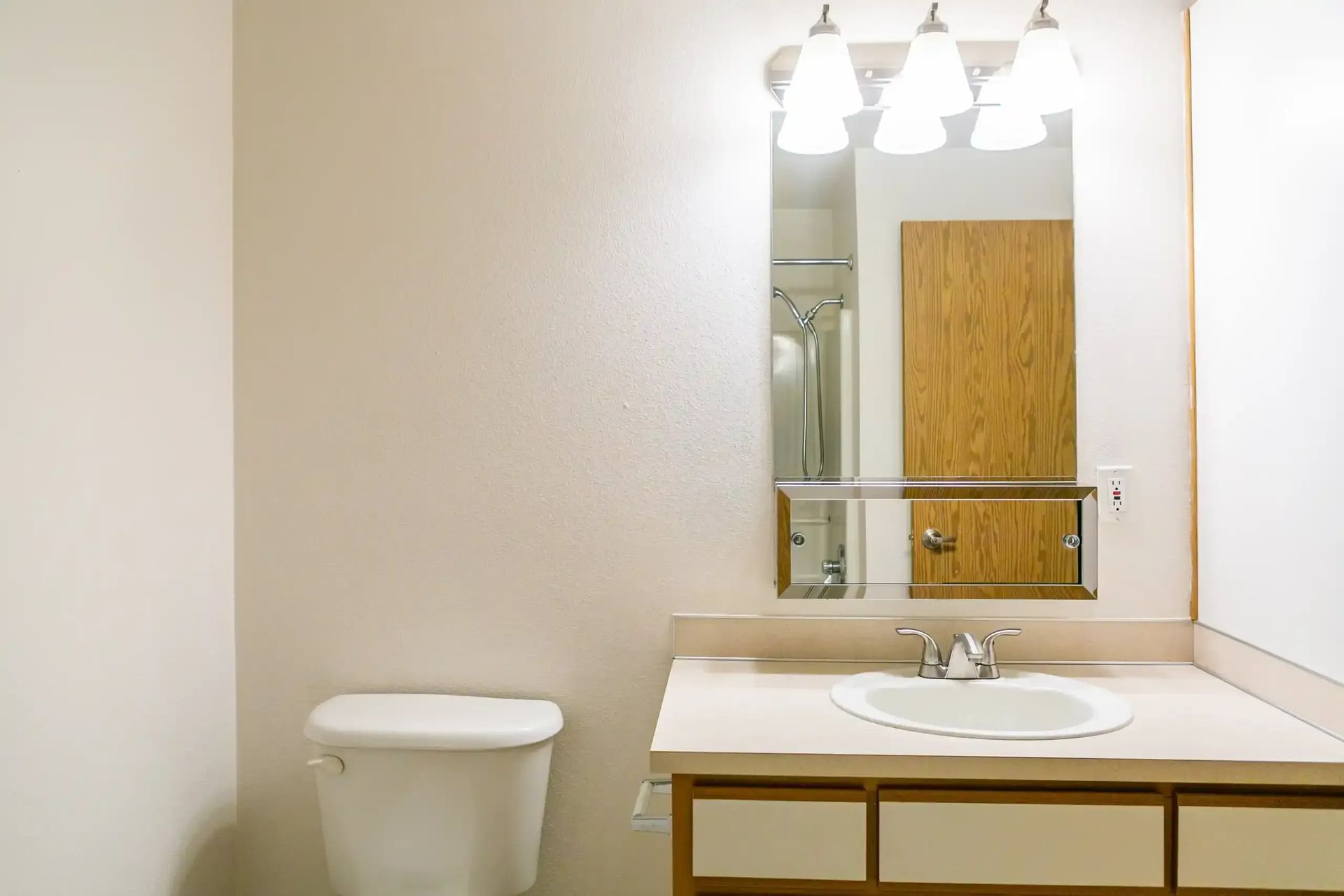 Bathroom vanity with sink, mirror, light fixture, and toilet in a beige room